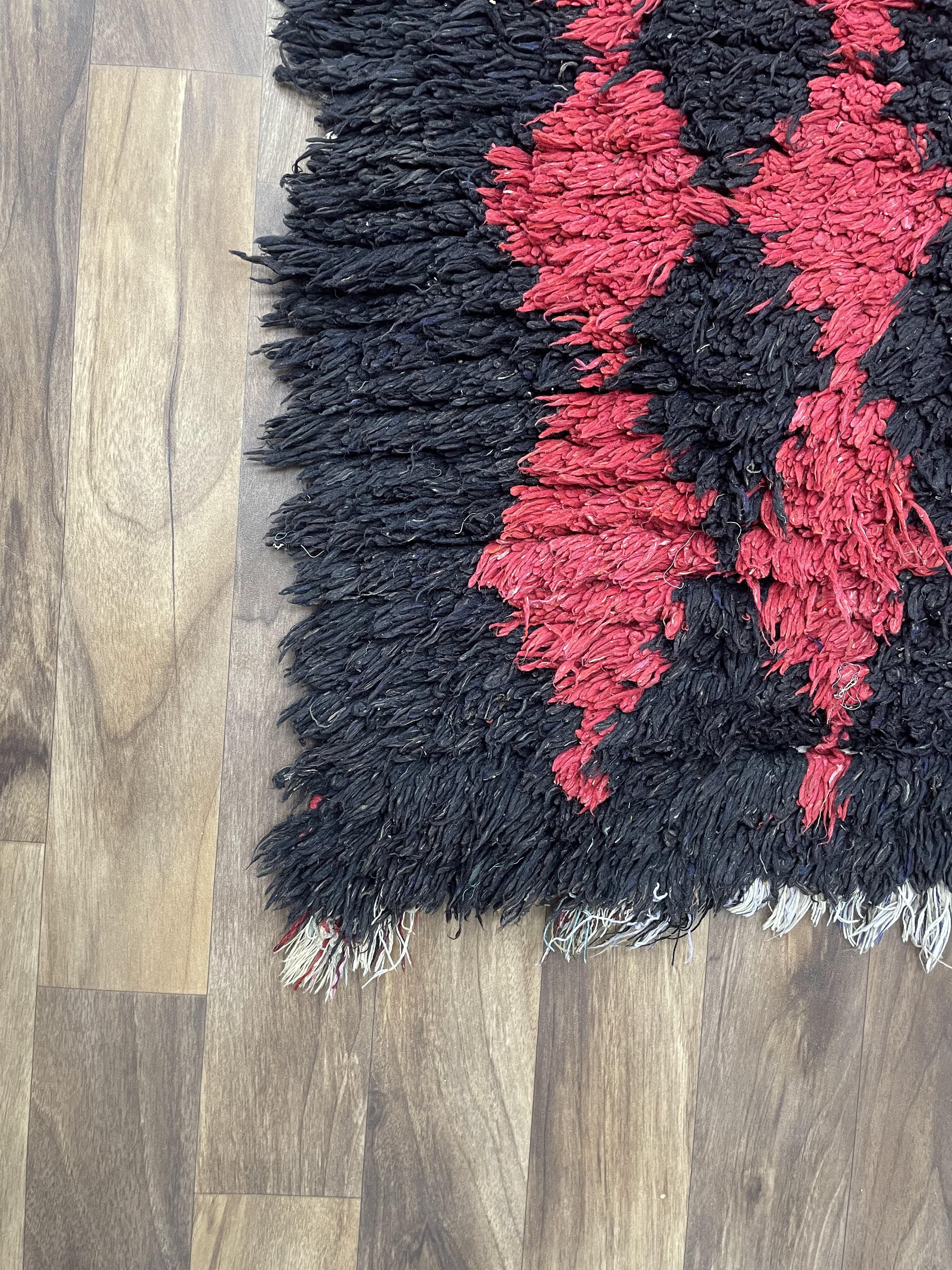 Textured black and red rug on wooden floor, ideal for enhancing home decor.