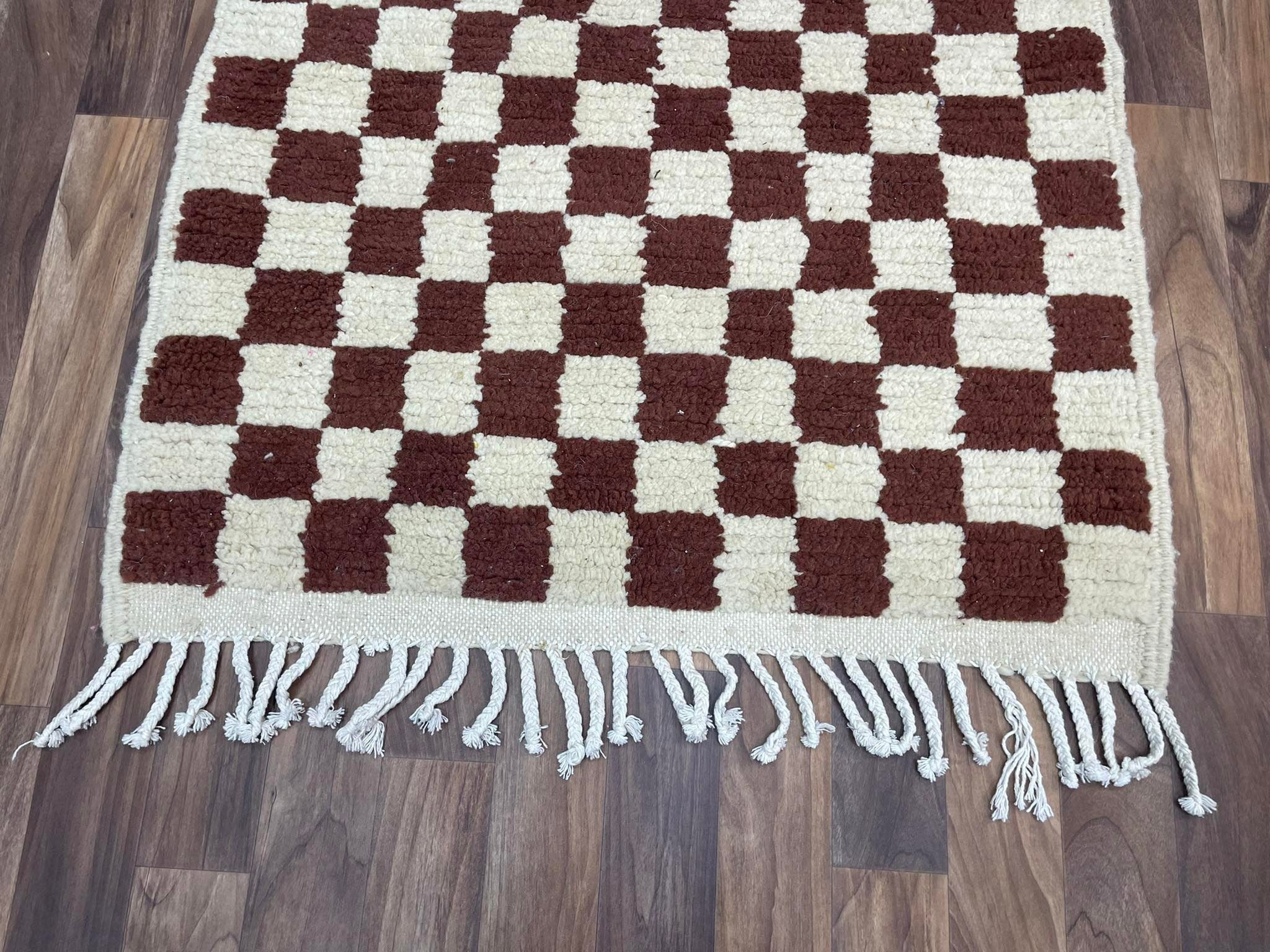 Brown and cream checkered rug with fringes, adding style and comfort to any space.