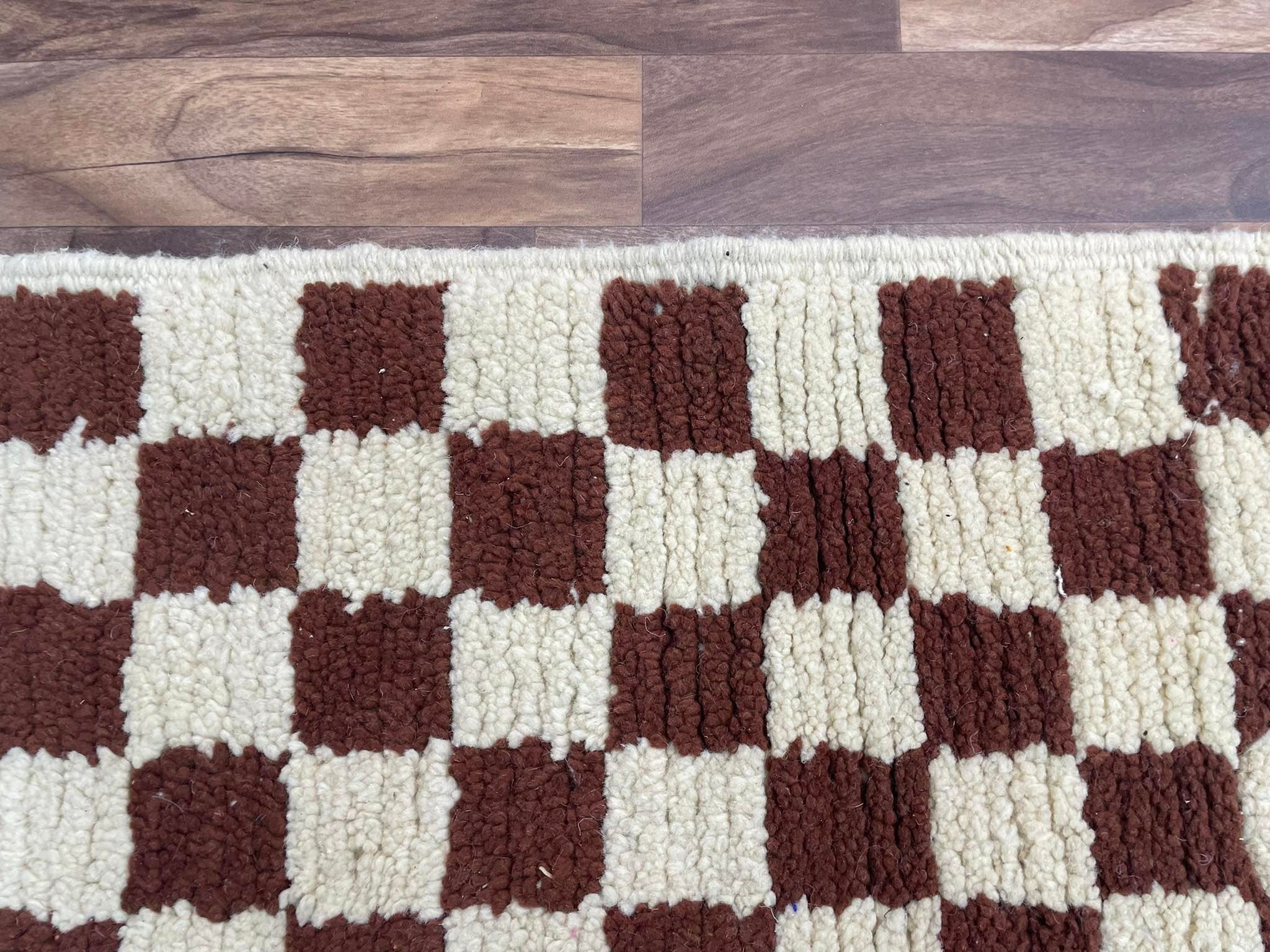 Brown and cream checkerboard area rug on wooden floor, perfect for home decor.